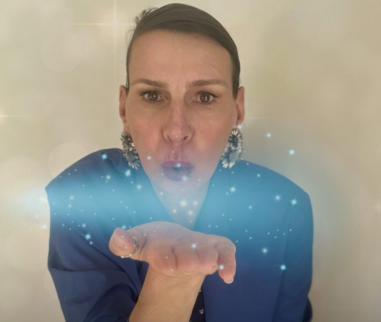Ellen mit großen Ohrringen, bläst funkelnde Partikel aus der Hand.