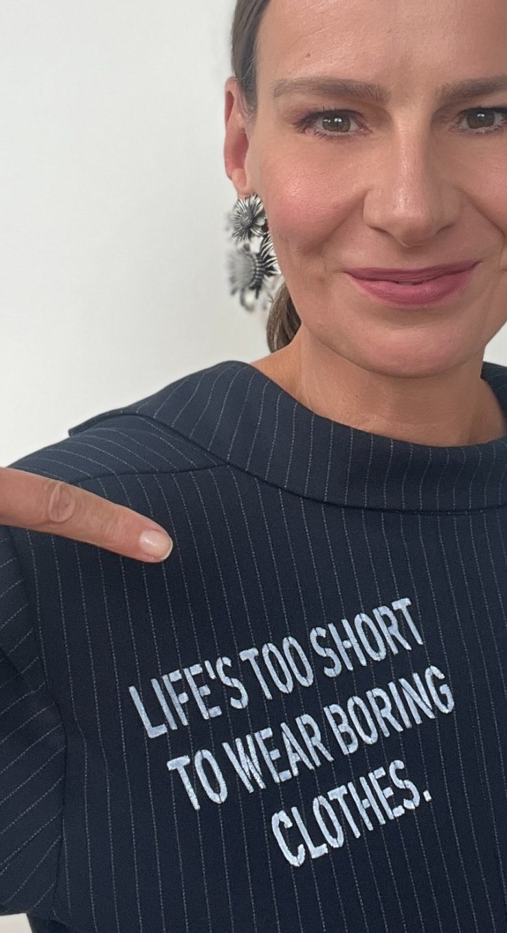 Ellen Schmitt zeigt auf ihr Oberteil mit dem Spruch „Life's too short to wear boring clothes.“