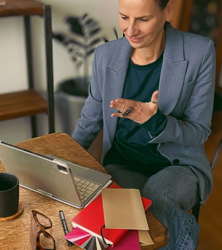 Strahlen mit Stil. Ellen Schmitt in blauem Blazer sitzt an einem Tisch mit Laptop und Notizbuch bei einer Beratung.
