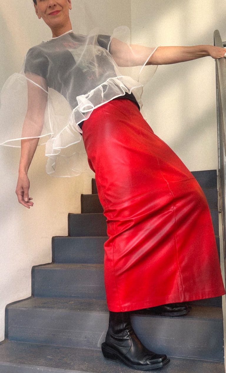Authentisch aussehen und fühlen Ellen Schmitt in rotem Lederrock, grauem Oberteil und schwarzer Stiefel, steht auf einer Treppe.