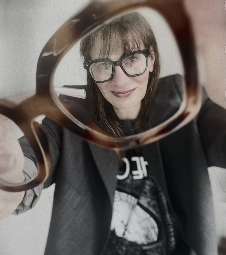 Ellen Schmitt guckt durch eine Brille, die sie wie ein Vergrößerungsglas hält.