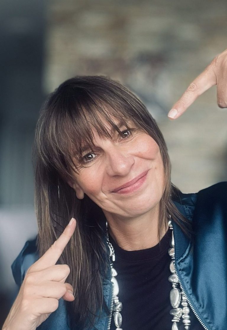Ellen Schmitt zeigt mit beiden Zeigefingern auf ihr Gesicht.